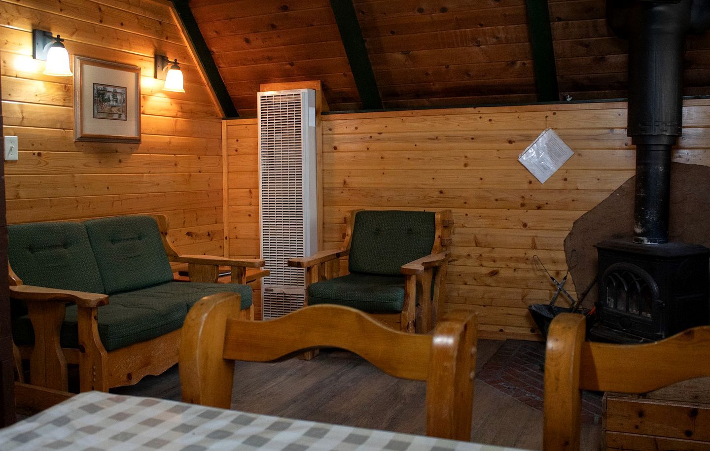 Een gezellig houten interieur met een open haard en twee groene fauteuils.