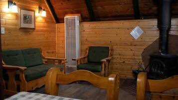 Een gezellig houten interieur met een open haard en twee groene fauteuils.