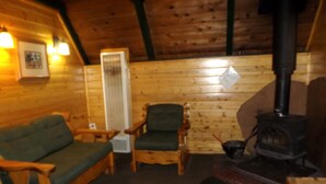 Ein gemütliches Blockhaus-Interieur mit einer Holzsofa, einem Sessel, einem Heizgerät und einem Kamin.
