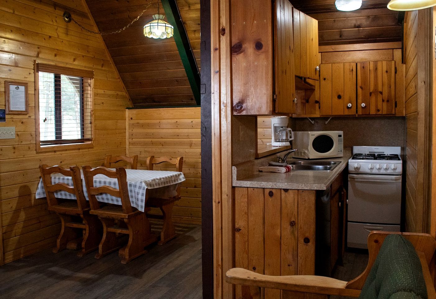 Interior de una cabaña de madera con comedor, cocina y una ventana con persianas.