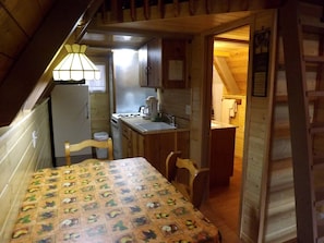 Une cuisine compacte avec des meubles en bois, un réfrigérateur, un évier et une table recouverte d’une nappe à motifs de fruits.