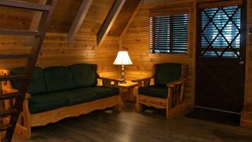 Een gezellig blokhutinterieur met een houten trap, een groene bank, een houten tafel met een lamp en een deur met een raam.