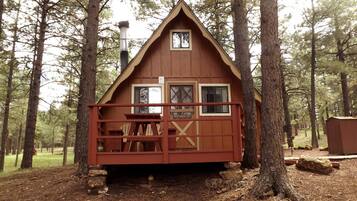 Une cabane en bois avec un porche à l’avant, une cheminée et une fenêtre.