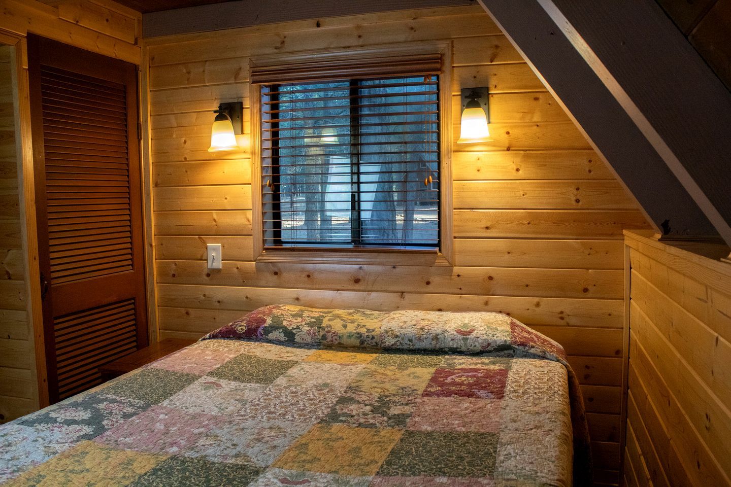 Ein gemütliches Zimmer mit einem Bett, einem Fenster mit Jalousien und zwei Wandleuchten.