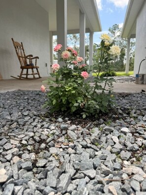 Ein Gartenbereich mit Kiesbeeten, einem hölzernen Schaukelstuhl und einer Veranda mit Säulen.