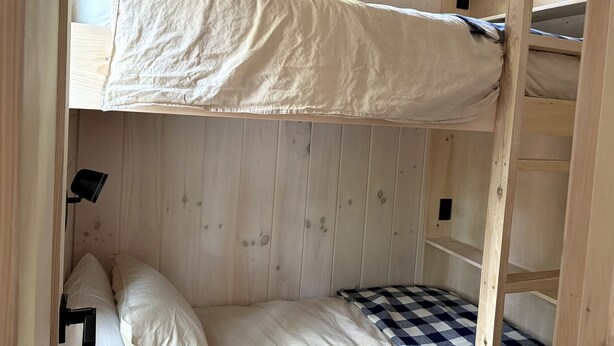 Un letto a castello con materasso a quadretti, pareti di legno e un piccolo ripiano.