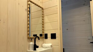 A bathroom with a wooden wall, a sink with a black faucet, a mirror, and a toilet.