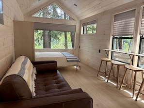 A cabin interior with a loft bed, a brown leather sofa, and a dining area with stools.