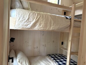 Een stapelbed met een geruit matras, houten wanden en een klein plankje.