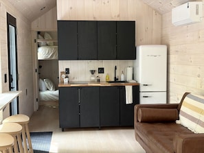 A compact room with a kitchenette, a bed, a brown leather sofa, and a small dining area.