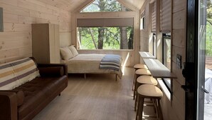 A wooden cabin interior with a bed, a sofa, and a dining area.