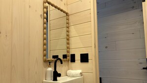 Un bagno con parete in legno, un lavandino con rubinetto nero, uno specchio e un water.