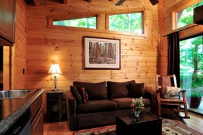 L’intérieur d’un chalet en bois comprend un canapé, une photographie de forêt encadrée, un coin repas et une fenêtre donnant sur les arbres.