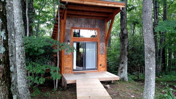 Une cabane en bois avec une porte en verre, entourée d’arbres.
