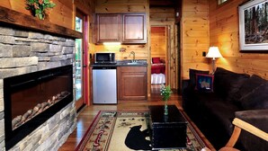 Een knus cabin interieur met een stenen open haard, houten wanden, een keukenhoek en een woonkamer met een bank en een lamp.