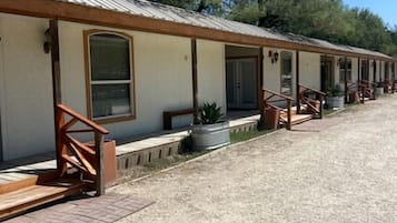 A row of motel rooms with individual entrances, outdoor seating, and a gravel driveway.