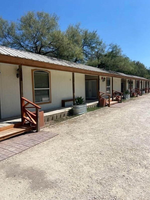 Filas de habitaciones de motel con entradas individuales, zonas de estar al aire libre y un camino de grava.