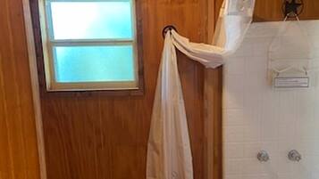 A wooden bathroom with a toilet, a shower, and a window.