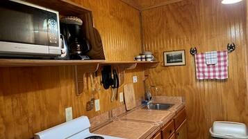A compact kitchen with wooden walls, a white stove, a microwave, a sink, and a trash bin.