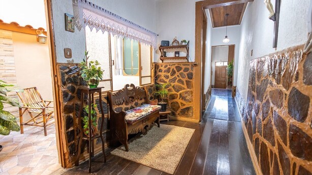 A hallway with a stone wall, a wooden bench, a potted plant, and a door leading to another room.