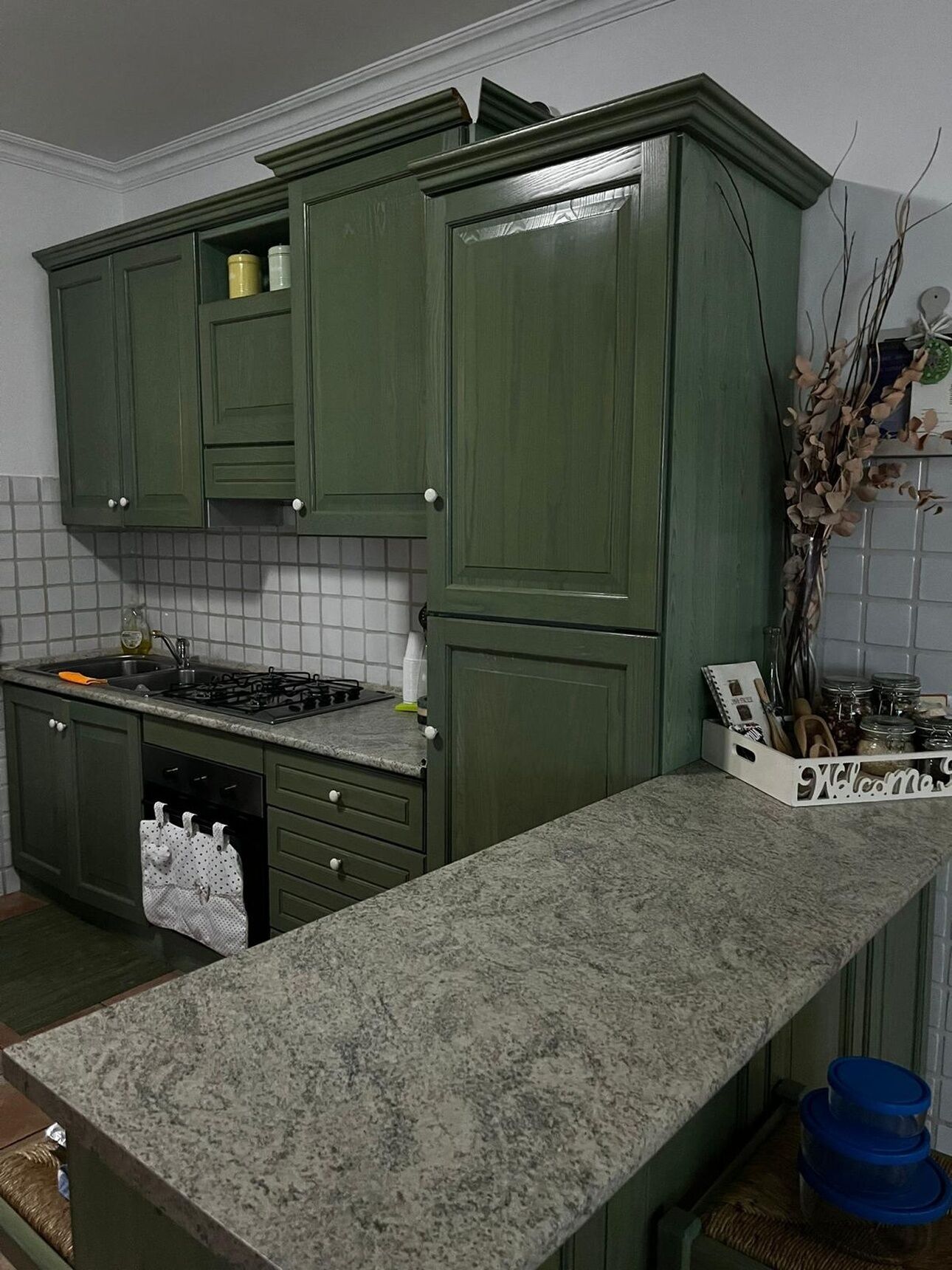 A kitchen with green cabinets, a granite countertop, a stove, and a dish rack.