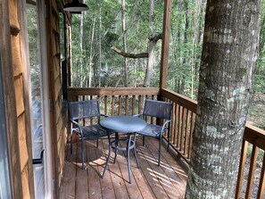 Une terrasse en bois avec une table et deux chaises, entourée d’arbres.