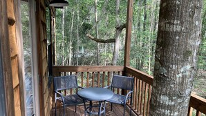 A wooden deck with a table and two chairs, surrounded by trees. - Cozy Tree House with Beautiful Modern Interior in Livingston, Texas (Livingston)