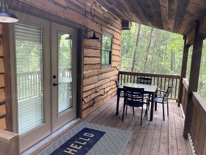 Une terrasse en bois avec une table et des chaises, une porte avec un panneau en verre et un paillasson sur lequel est écrit « BONJOUR ».