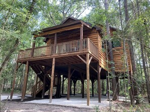 Une cabane en bois dotée d’un balcon, construite sur pilotis dans une zone boisée.