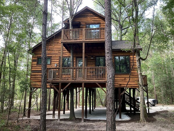 Une cabane en bois dotée d’un balcon à l’étage, entourée d’arbres.