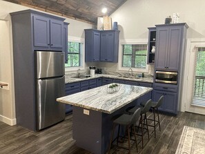 A modern kitchen with dark blue cabinets, a stainless steel refrigerator, a marble island, and a built-in oven. - Cozy Tree House with Beautiful Modern Interior in Livingston, Texas (Livingston)