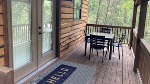 A wooden deck with a table and chairs, a door with a glass panel, and a 'HELLO' mat. - Cozy Tree House with Beautiful Modern Interior in Livingston, Texas (Livingston)