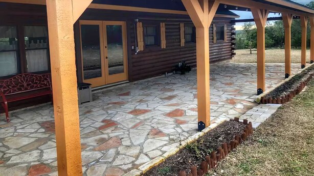Un patio cubierto con suelo de piedra, vigas de madera y un banco.