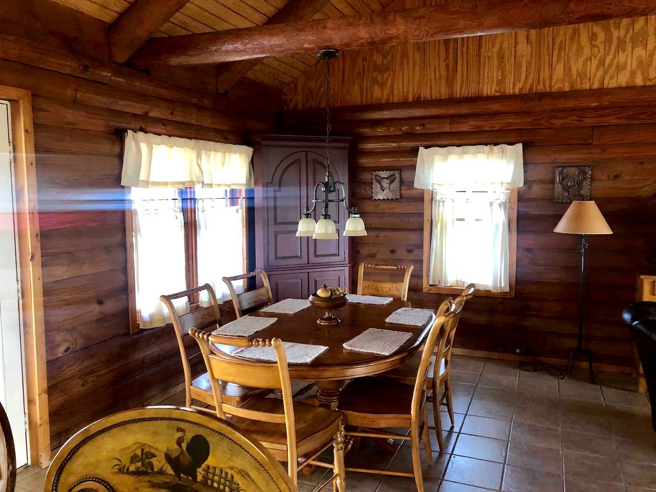 A wooden dining room with a round table, chairs, and a chandelier.
