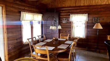 A wooden dining room with a round table, chairs, and a chandelier.