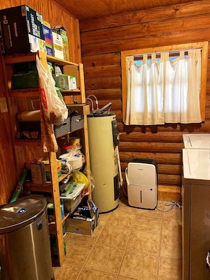 Pieni, käytännöllinen keittiö, jonka seinät ovat puuta. Keittiössä on jääkaappi, mikroaaltouuni, pesuallas ja ikkuna, jossa on verhot.