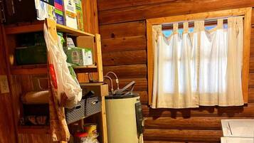 A compact kitchen with wooden walls, a refrigerator, a microwave, a sink, and a window with curtains.