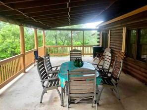 Un patio techado al aire libre con una mesa redonda y cuatro sillas, rodeado por una barandilla de madera.