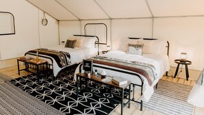 A tent-style room with two beds, a small table, and a lamp. - Lake Blackshear Glamping Retreat: Cozy Safari Tent in Cordele, Georgia (Cordele)