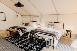 Een tent-achtige kamer met twee bedden, een tafeltje en een lamp.