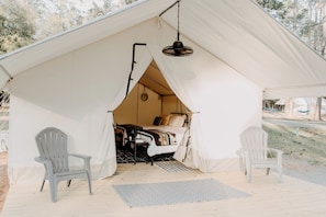 A tent with a bed, two chairs, and a hanging light fixture.