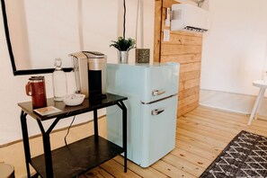 Eine kompakte Küchenzeile mit Kaffeemaschine, kleinem Kühlschrank und einem Tisch mit Tasse und Schüssel.