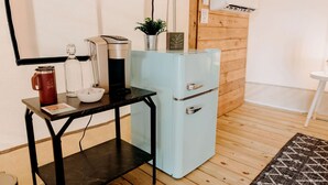A compact kitchenette with a coffee maker, a small fridge, and a table with a mug and a bowl. - Lake Blackshear Glamping Retreat: Cozy Safari Tent in Cordele, Georgia (Cordele)