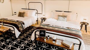 A tent-style room with two beds, a small table with a sign, and a patterned rug. - Lake Blackshear Glamping Retreat: Cozy Safari Tent in Cordele, Georgia (Cordele)
