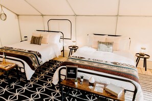 Een tentvormige kamer met twee bedden, een klein tafeltje met een bord en een kamerbreed tapijt met een patroon.