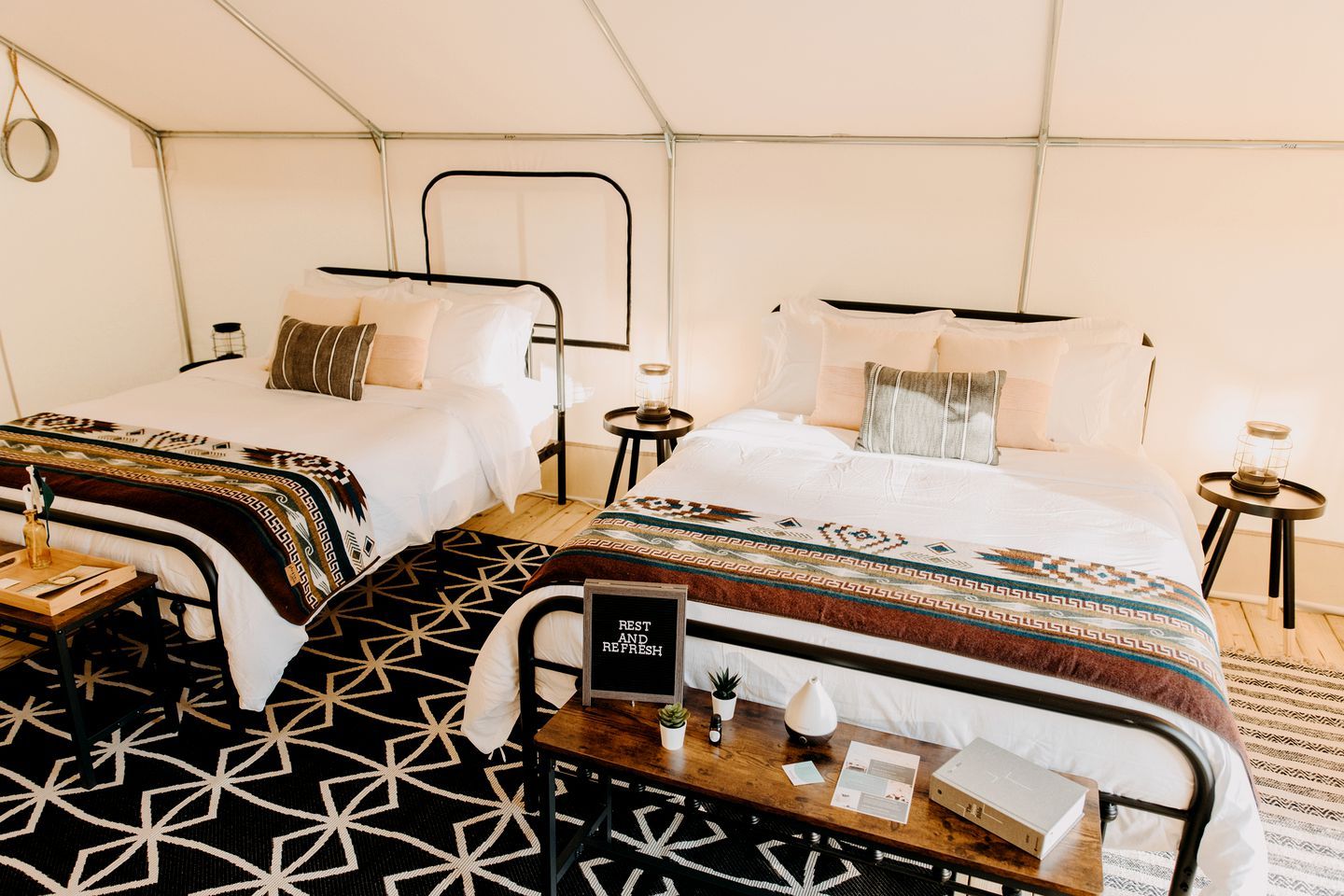 Een tentvormige kamer met twee bedden, een klein tafeltje met een bord en een kamerbreed tapijt met een patroon.