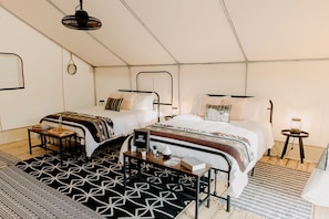 A tent-style room with two beds, a small table, and a lamp.