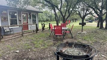A backyard with a fire pit, red chairs, and a small building with windows and a door.