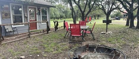 A backyard with a fire pit, red chairs, and a small building with windows and a door.