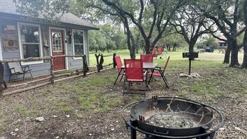 A backyard with a fire pit, red chairs, and a small building with windows and a door.